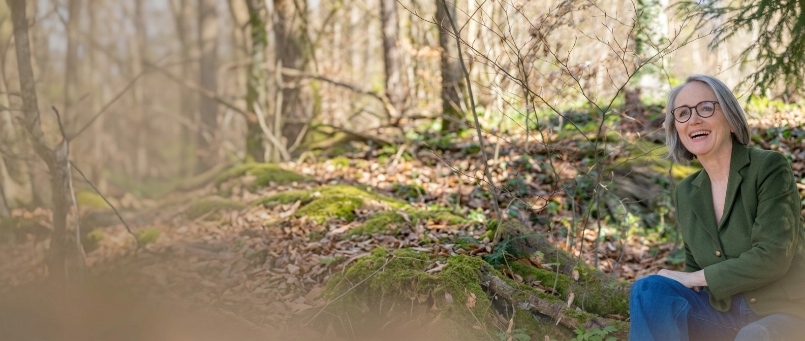 Ute Hefel, lachend im Wald sitzend